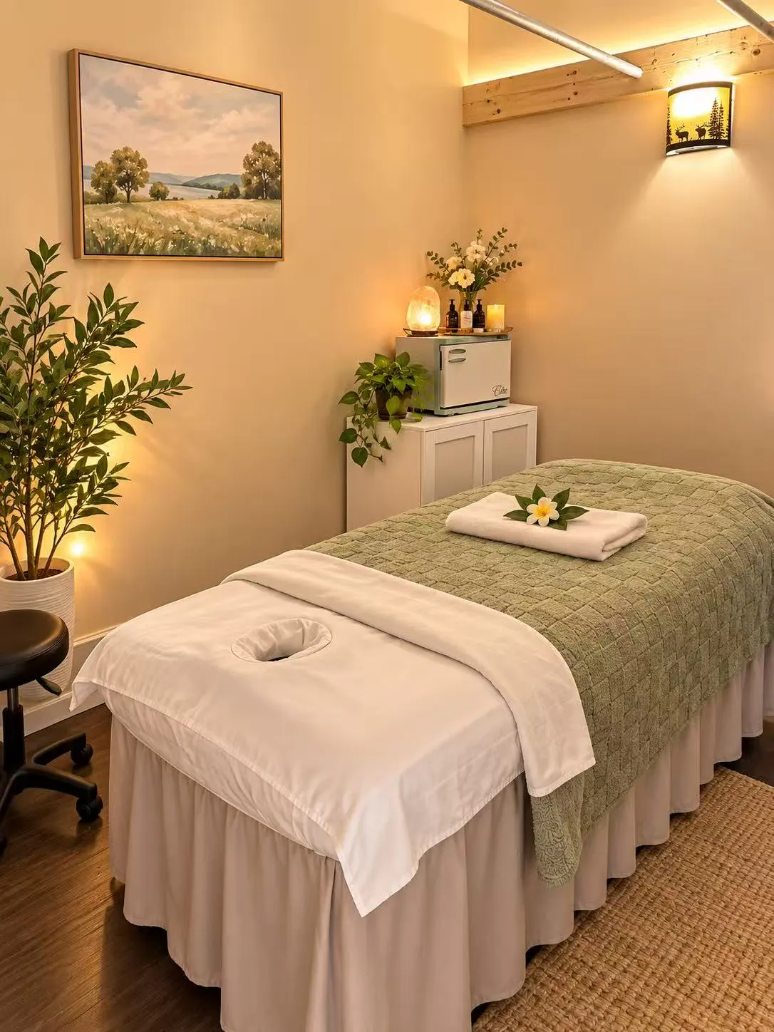 Massage table with a face cradle and sage blanket, a leafy tree in a white planter beside it